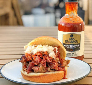 Pulled pork BBQ sandwich with coleslaw and BBQ Buddha Memphis Mop sauce on a plate outdoors