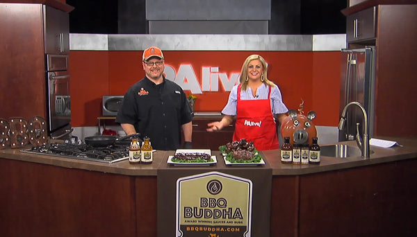 Chef and TV host in studio kitchen with BBQ Buddha sauces and grilled meats on display