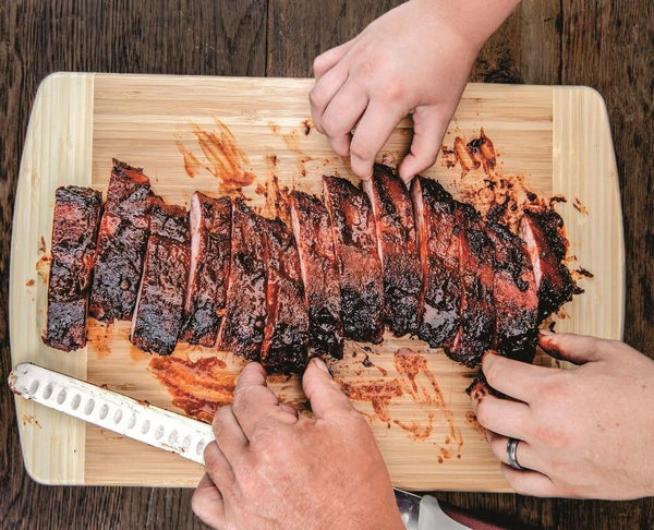 Slow-smoked Memphis style barbecue ribs sliced on a wooden cutting board, hands serving