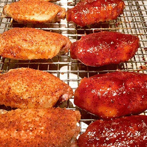 Two styles of seasoned chicken wings, dry rub and sauced, on a wire rack for grilling